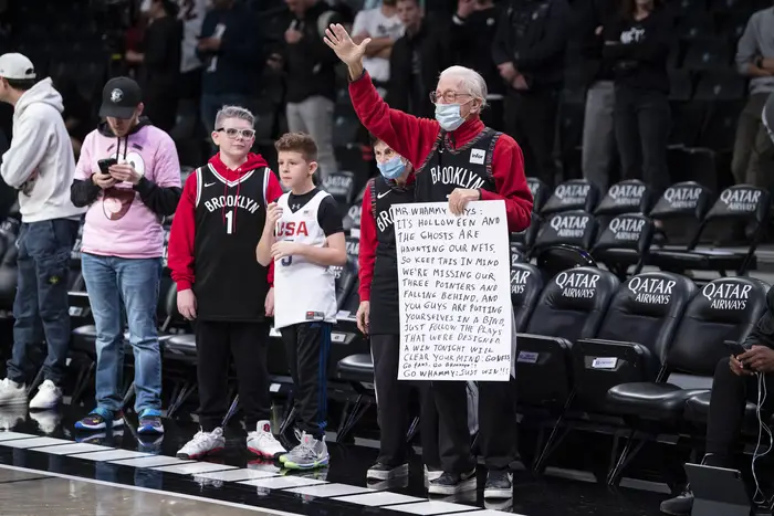 Brooklyn Nets fans standing courtside. A elder fan holds a handwritten sign.
